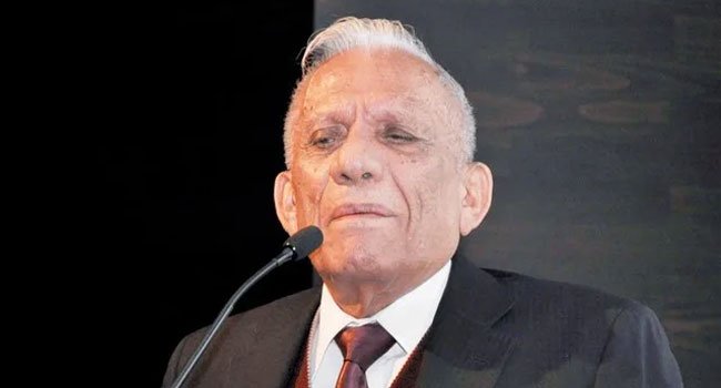 صورة قريبة للشاعر العراقي الراحل عبد الرزاق عبد الواحد يرتدي بدلة رسمية ويتحدث أمام الميكروفون بملامح متأثرة ومليئة بالحنين.
