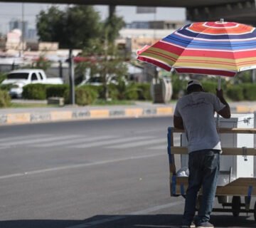 بائع متجول يستظل بمظلة ملونة في أحد شوارع بغداد
