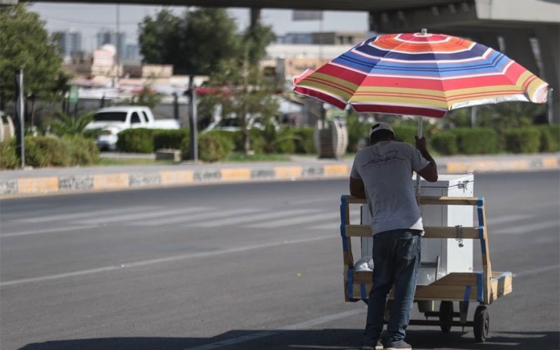 بائع متجول يستظل بمظلة ملونة في أحد شوارع بغداد
