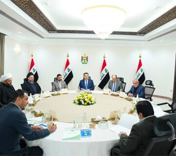 اجتماع رسمي يضم عدداً من المسؤولين العراقيين حول طاولة اجتماعات بحضور الأعلام العراقية 