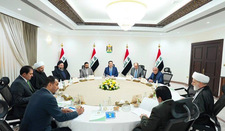 اجتماع رسمي يضم عدداً من المسؤولين العراقيين حول طاولة اجتماعات بحضور الأعلام العراقية.