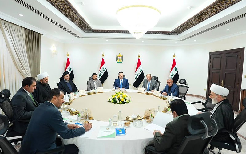 اجتماع رسمي يضم عدداً من المسؤولين العراقيين حول طاولة اجتماعات بحضور الأعلام العراقية 