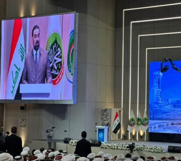 هیبت-الحلبوسي الحلبوسي يلقي كلمة في مؤتمر رسمي خلفه شاشة بعلم العراق