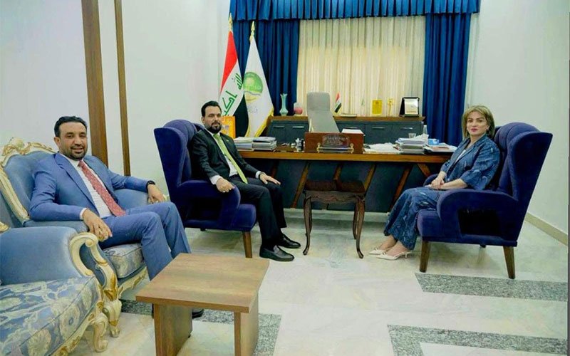 لقاء رسمي في مكتب شبكة الإعلام العراقي يجمع رجلين وامرأة يناقشون تعزيز التوعية البيئية 