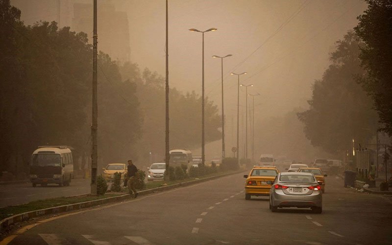 شارع في العراق مغطى بالغبار الكثيف مع تدني الرؤية وحركة سيارات وسط أجواء مغبرة 