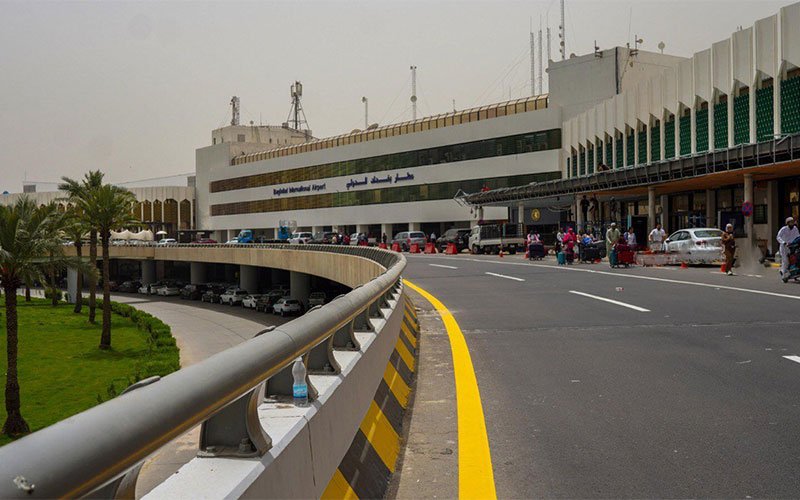 تُظهر الصورة مبنى مطار عراقي ومنطقة مخصصة لوصول ومغادرة المسافرين وسط حركة المركبات أمام صالات المطار 